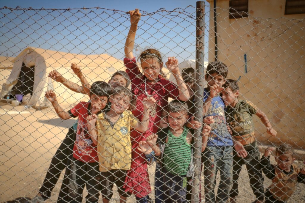 Children gather behind a fence in a refugee camp in Idlib, Syria, highlighting the challenges faced by refugees.